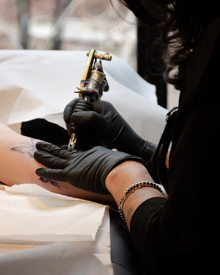 Tattoo artist in black gloves holding a coil machine while working on a client's arm